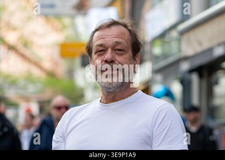 Ein 50-jähriger Mann in weißem T-Shirt steht auf der Stadtstraße und schaut in die Kamera. Stockfoto