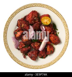 Scharfe rote gebratene Hähnchenstücke auf Keramikplatte isolierter weißer Hintergrund, Zwiebelringe Limetten- und Curryblätter, Blick von oben, indisches Küchenkonzept Stockfoto