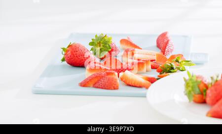 In Scheiben geschnittene und ganze Erdbeeren ordentlich auf einem blauen Schneidebrett angeordnet. Stockfoto
