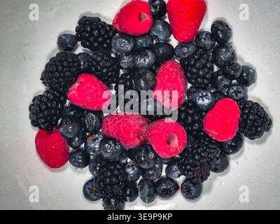 Blick von oben nach unten auf einen Haufen frischer Himbeeren, Heidelbeeren und Brombeeren in einer sauberen weißen Schüssel. Minimalistische Lebensmittelfotografie für gesunde Ernährung Conce Stockfoto