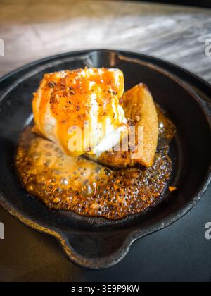Ein warmer Dessertkuchen oder Keks, serviert in einer gusseisernen Pfanne, gekrönt mit einer Schaufel Eis, Karamell-Nieseln und Nüssen. Stockfoto