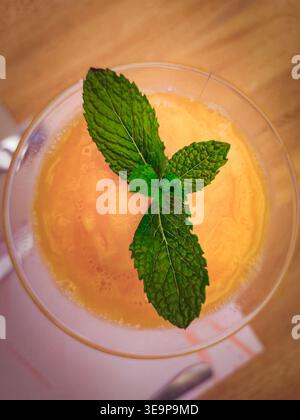 Hochwinkelansicht eines gefrorenen Orangengetränks, garniert mit frischen Minzblättern in einem Glas. Sommererfrischung auf Holztisch. Stockfoto