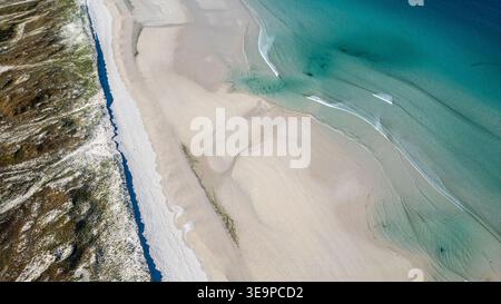 Top-Down-Luftaufnahme, die den unglaublichen Kontrast zwischen dem feinen weißen Sand und den türkisfarbenen Tönen des Atlantiks einfängt. Lichtwellen überlappen die s Stockfoto