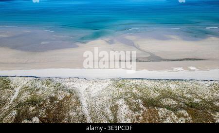 Top-Down-Luftaufnahme, die den unglaublichen Kontrast zwischen dem feinen weißen Sand und den türkisfarbenen Tönen des Atlantiks einfängt. Lichtwellen überlappen die s Stockfoto