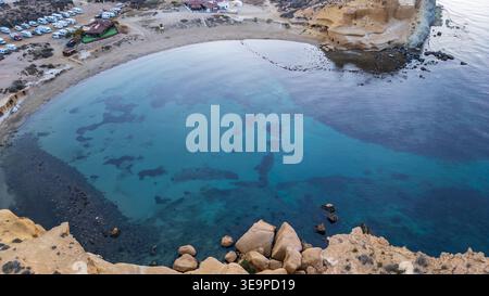 Zenital-Luftaufnahme von Playa de los Cocedores, Spanien. Das Bild zeigt das kristallklare Wasser einer Halbmondbucht, goldene Klippen und einen Parkplatz Stockfoto