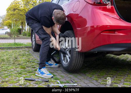 Mann, der das Autorad nach dem Reifenwechsel mit Werkzeugen auf dem Boden im Freien montiert Stockfoto