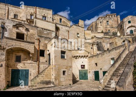 Besucher spazieren durch die engen Gassen der Altstadt von Matera. Historische Gebäude erheben sich vor einem blauen Himmel. Stufen führen zu versteckten Ecken. Stockfoto