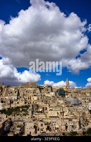 Matera zeigt seine einzigartigen Steinbauten unter einem blauen Himmel mit Wolken. Die Stadt blickt auf Landschaften und historische Bauten. Stockfoto