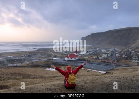 Rückansicht eines Touristen, der den Blick auf die Reyniskirkja Kirche zwischen den Bergen in der Nähe des Strandes im Sommer in der Stadt Vik, Südisland, bewundert. Stockfoto