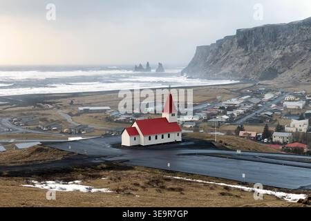 Panoramablick auf Basaltstacks Reynisdrangar, vulkanischer schwarzer Sandstrand mit Myrdal-Kirche, Island Stockfoto