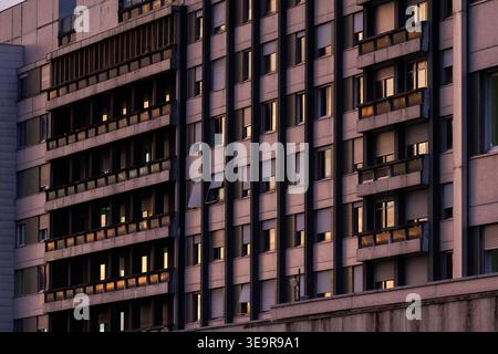Eine Nahaufnahme eines zeitgenössischen Apartmentkomplexes mit Balkonen, die das Spiegelbild der Sonne der goldenen Stunde in den Fenstern zeigt. Stockfoto