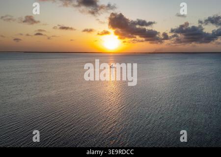 Panoramablick auf einen goldenen Sonnenuntergang über dem Indischen Ozean mit einem einsamen Segelboot auf dem glitzernden Wasser in Sansibar, Tansania Stockfoto
