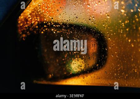 Regentropfen auf Autofenster und Seitenspiegel mit City-Nachtlichtern und Bokeh-Reflexen, selektiver Fokus Stockfoto