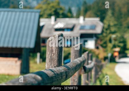 Hölzerne Barriere in einem slowenischen Alpendorf, mit traditionellen Häusern im Hintergrund, die außer Fokus stehen, symbolisieren ländlichen Lebensstil und Alpenbogen Stockfoto