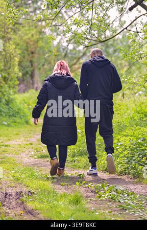 Ein Paar spaziert Hand in Hand auf einem grünen Pfad in einem Park an einem sonnigen Frühlingstag Stockfoto