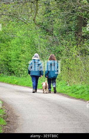 Zwei Frauen gehen tagsüber mit ihrem Hund auf einem Weg in einem grünen Bereich Stockfoto