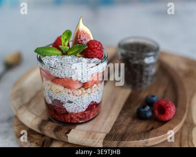 Vorderansicht des Chia-Parfait mit Beeren, Minze und Müsli auf Holzbrett in Naturtönen Stockfoto