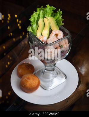 Die Glasschale bietet Platz für frische Garnelen, Avocado und Salat. Garnelen wirken prall und lebhaft, umgeben von knusprigem Grün. Runde, goldbraune Brotauflagen besi Stockfoto