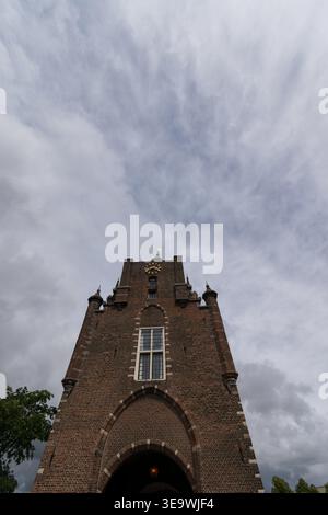 Flacher Blick auf den gemauerten Torturm mit Zifferblatt unter dramatischem bewölktem Himmel in Haarlem, Niederlande. Historische Architektur gegen stimmungsvolle Wolken. Stockfoto
