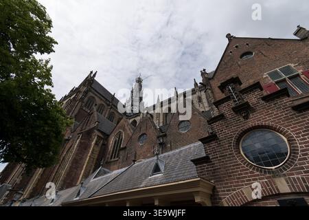 Flache Außenansicht der Grote Kerk (St. Bavo) in Haarlem, Niederlande, mit gotischem Turm und Ziegelfassade vor bedecktem Himmel. Stockfoto