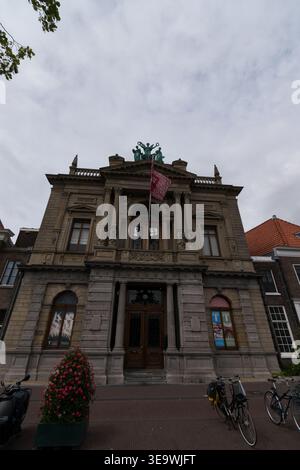 Neoklassizistische Fassade des Teylers Museum in Haarlem, Niederlande, mit symmetrischen Steinsäulen, Bronzeskulpturen und roter Flagge unter Überkappen Stockfoto