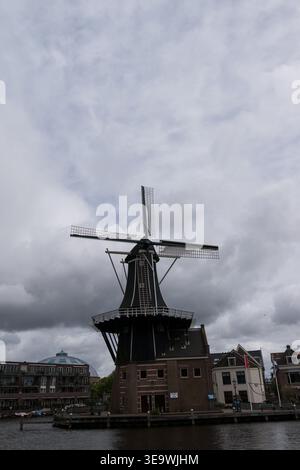 De Adriaan Windmühle am Fluss Spaarne in Haarlem, Niederlande, unter starkem bewölktem Himmel mit dramatischen Wolkenformationen. Stockfoto