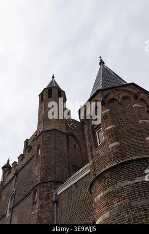 Flacher Blick auf zwei Backsteintürme mit konischen Türmen in der Grote Kerk in Haarlem, Niederlande. Bedeckter Himmel und architektonische Details sichtbar. Stockfoto
