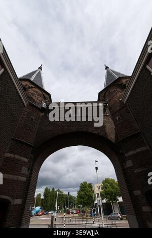 Blick durch den Backsteinbogen des Stadttors Amsterdamse Poort in Haarlem, Niederlande, mit Twin-Türmen und bedecktem Himmel. Stockfoto