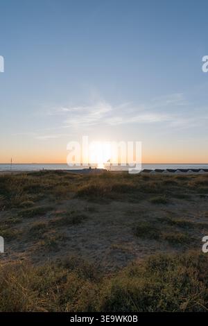 Sonnenuntergang über der Nordsee von den Küstendünen in Katwijk aan Zee, Niederlande. Strandhütten, die in der Abenddämmerung entlang der Küste zu sehen sind. Stockfoto