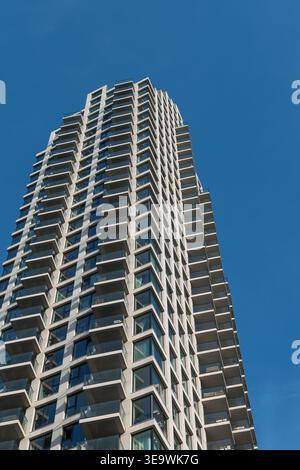 Zeitgenössischer Wohnturm mit geometrisch gestaffelten Balkonen vor klarem blauem Himmel in den Haag, Niederlande. Flacher Blick auf die Architektur. Stockfoto