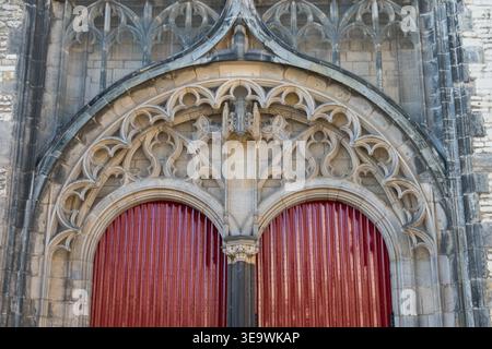 Gotisches Tracery-Portal mit verzierten Steinbögen und roten senkrechten Doppeltüren im Stadtteil Burcht in Leiden, Niederlande. Stockfoto