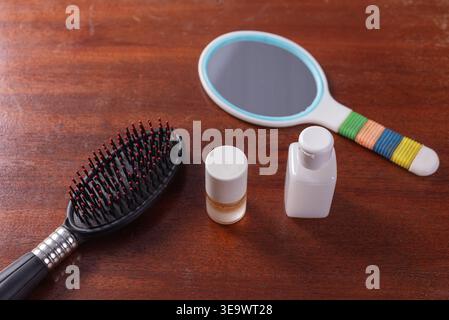 Nahaufnahme auf Holzoberfläche mit schwarzer Haarbürste, Handspiegel, zylindrischer und kleiner quadratischer Flasche. Konzentrieren Sie sich auf sanfte neutrale Beleuchtung und sm Stockfoto