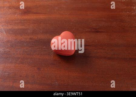 Studio-Aufnahme eines roten Herzens in Form eines Stressballs. Glatte Textur, indirekte Beleuchtung, auf dunkelbraunem Holzbrett. Konzeptionelle Aufnahme für Liebe, Sorgfalt oder Emoti Stockfoto