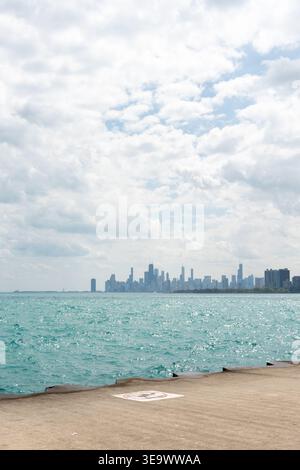 Vertikale Aufnahme von Chicagos Wolkenkratzern, die sich an einem sonnigen Tag über dem pulsierenden blauen Wasser des Lake Michigan erheben und das urbane Leben miteinander verschmelzen Stockfoto