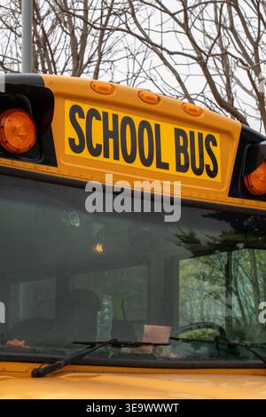 Vertikale Nahaufnahme des auffälligen „SCHOOL BUS“-Schriftstücks an der Seite eines ikonischen gelben Schulbusses, ein vertrauter Anblick, der den sicheren Transport gewährleistet Stockfoto