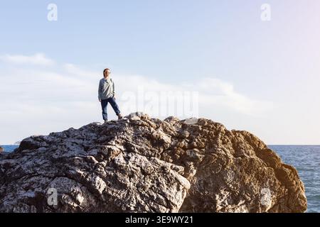 Frau, die auf einer felsigen Klippe steht und den Horizont überblickt. Stockfoto
