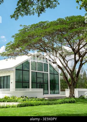 Modernes minimalistisches Haus mit großen Glasfenstern, umgeben von grünem Garten und Bäumen. Umweltfreundliches Wohnen, natürliches Lichtdesign, nachhaltiges lifestyl Stockfoto