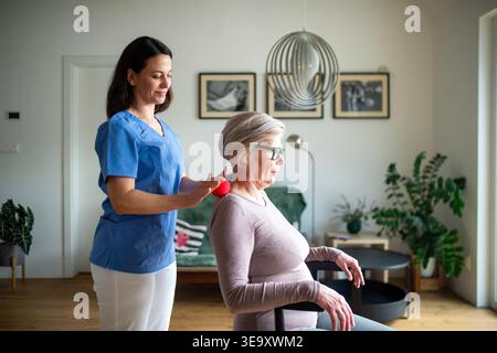 Pflegekraft hilft älteren Frauen bei Rehabilitationsübungen mit Massageball. Stockfoto
