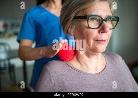Pflegekraft hilft älteren Frauen bei Rehabilitationsübungen mit Massageball. Stockfoto