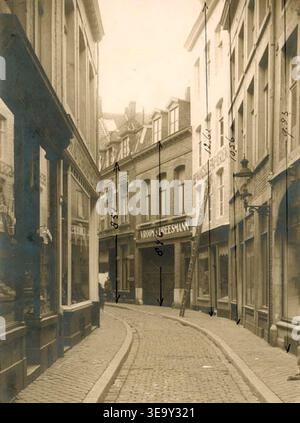 Dieses Foto, das zwischen 1925 und 1930 in Maastricht aufgenommen wurde, zeigt die Vijfharingenstraat vor dem Abriss der Gebäude auf der ungeraden Seite (rechts) für den Bau eines Vroom & Dreesmann-Geschäfts. Die Höhe der Gebäude ist bis zur Dachlinie markiert. Stockfoto