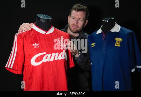 Ein Mitarbeiter von Propstore sieht sich Steve Nikols Match-getragenes Scotland gegen England 1988 Rous Cup Trikot (EST 1.000–£ 2.000) zusammen mit seinem Match getragenen Liverpool gegen Everton 1989 FA Cup Abschlussshirt (EST 3.000–£ 6.000) an, während er eine Vorschau auf den bevorstehenden Steve Nicol-Verkauf im Propstore in Rickmansworth, Hertfordshire, vorstellt 0001. Bilddatum: Dienstag, 14. April 2026. Stockfoto