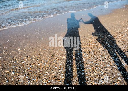 Silhouette Schatten von zwei Personen, die Hände auf Muschelstrand mit Meereswellen gegossen halten Stockfoto