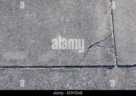 Graue Betonpflasterstruktur mit tiefem Riss auf der Oberfläche, die Schäden zeigt und verwitterte Gehsteige, die sich vernachlässigt und in einem leeren Raum verlassen fühlen Stockfoto