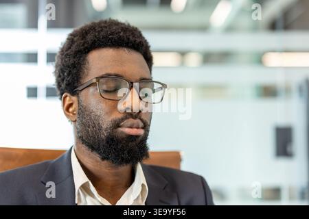 Geschäftsmann mit geschlossenen Augen, der sich während einer Pause entspannt, im Büro Seelenruhe und geistige Klarheit findet, Achtsamkeit und Stressabbau üben, um Wohlbefinden und Konzentration zu verbessern Stockfoto