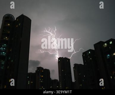 Ein kräftiger Blitz beleuchtet dunkle Stadtgebäude während eines dramatischen Nachtsturms Stockfoto