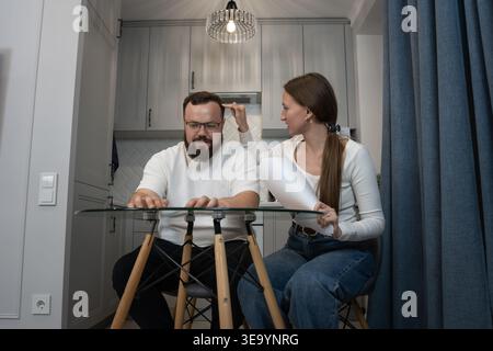 Junges Paar am Küchentisch, das sich über Finanzdokumente, Budget, Steuern und Hypotheken dreht, während es von zu Hause aus arbeitet - durchdachtes, fokussiertes Haus Stockfoto