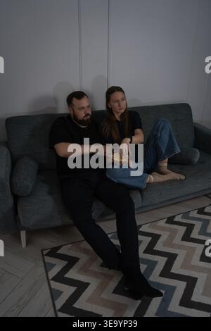 Paare entspannen auf einer Couch in einem dunklen Raum und schauen Fernsehen, genießen Snacks und verbringen einen Abend zusammen in einem zwanglosen und komfortablen Haus Stockfoto