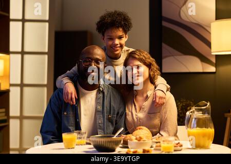Porträt einer vielfältigen Familie, die am Esstisch lächelt und umgeht, zeigt Verbundenheit und moderne Elternschaft. Ideal für Erziehungskampagnen, Familienmarketing, Medium Shot Stockfoto