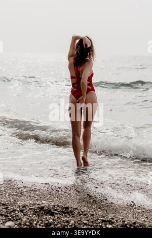 Badeanzüge für Frauen, die in der Brandung an einem Strand stehen, während sie auf das Meer blicken, während eines ruhigen Sommerurlaubs Stockfoto
