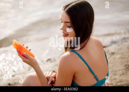 Frau, die eine Sonnenschutzflasche hält und das Produkt ansieht. Hautpflege und Sonnenschutz. Frau mit Sonnencreme mit Hautpflegeprogramm und kosmetischer Werbung Stockfoto